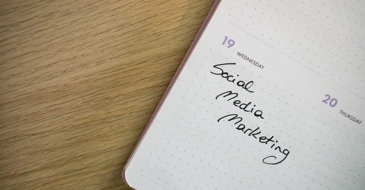 A dotted planner open on a wooden desk, with social media marketing handwritten under Wednesday the 19th.