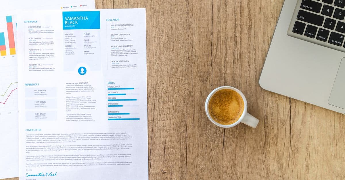 A printed CV with a skills section and a cover letter on a wooden desk, beside a cup of coffee and a laptop.