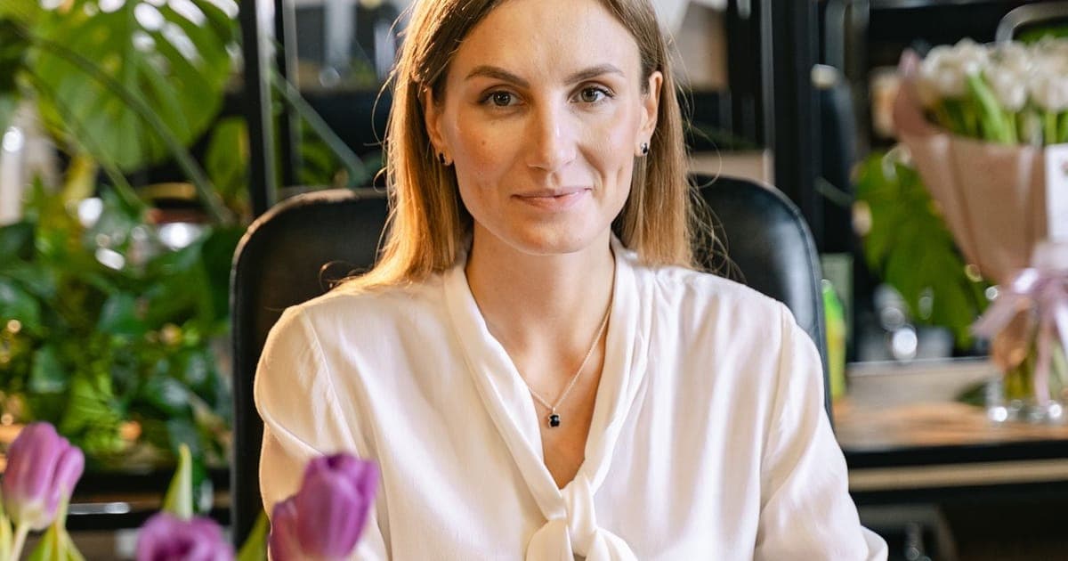 Woman at a bright, plant-filled desk with her laptop and printed charts