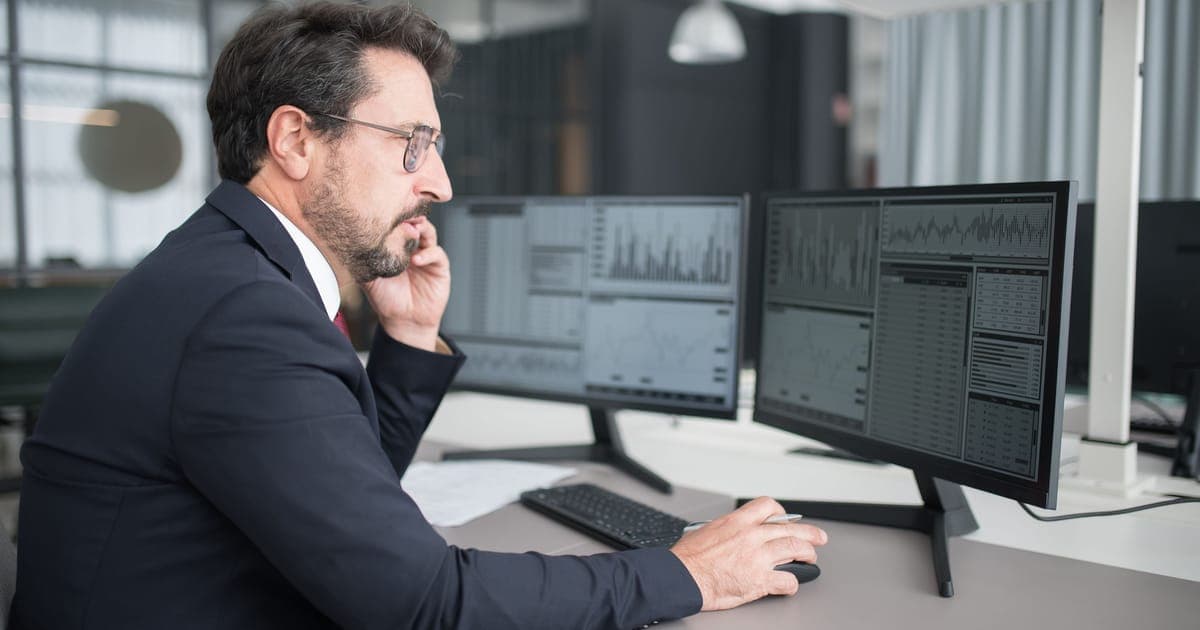 Analyst at two monitors showing bar charts and trend reports